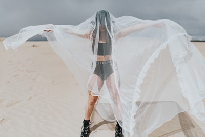 穿着白色婚纱和黑色皮靴站在白色沙滩上的女人